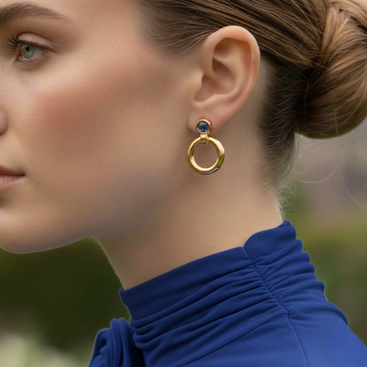 Model draagt minimalistische goudkleurige statement oorbellen met blauwe steen in vintage stijl.