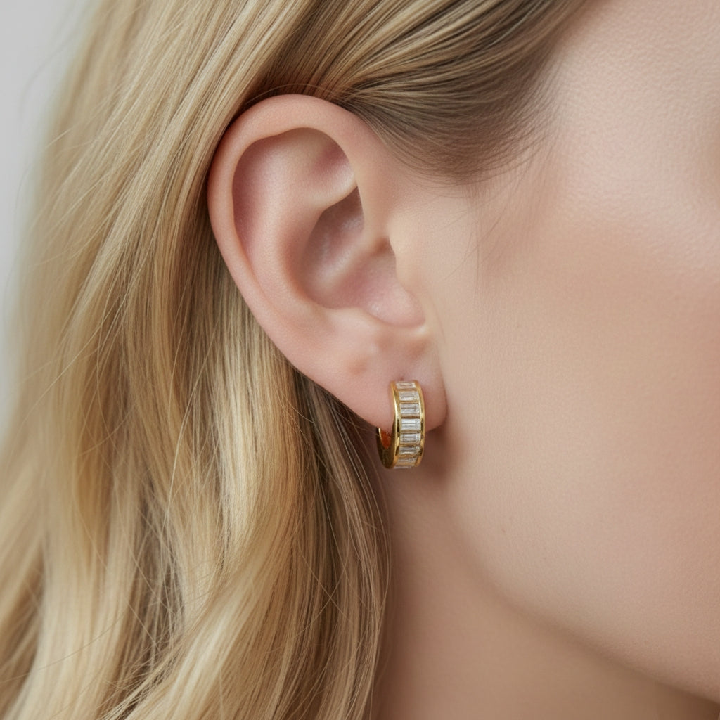 Model draagt minimalistische gouden creolen ingelegd met rechthoekige kristallen, moderne baguette-stijl oorbellen.