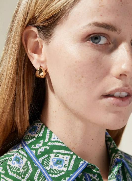 Model draagt minimalistische goudkleurige teardrop creolen in chunky design - de trend van dit seizoen.