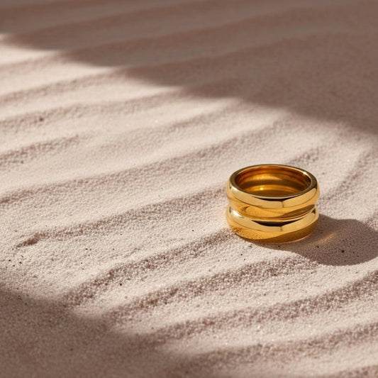 Gouden dubbele bolle ring van CECELYN in zand met zachte schaduwen.