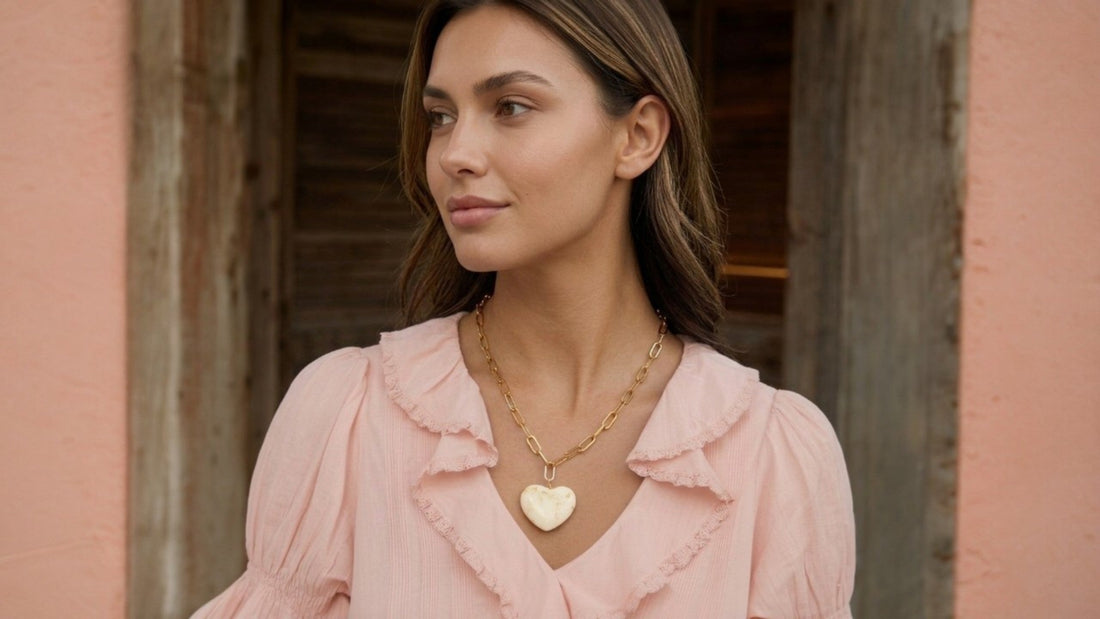 Jonge vrouw in roze blouse met gouden CECELYN-ketting en witte harthanger.