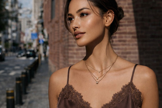 Jonge vrouw in een bruin satijnen top met een gelaagde gouden CECELYN-bolketting, vastgelegd op straat.