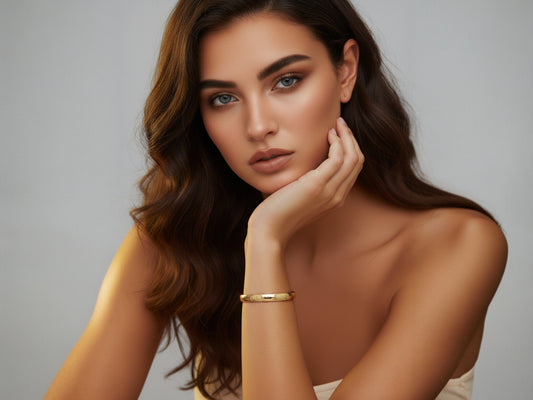 Jonge vrouw met bruine haren en blauwe ogen draagt een gouden armband van CECELYN, Valentijns sieradenfoto.
