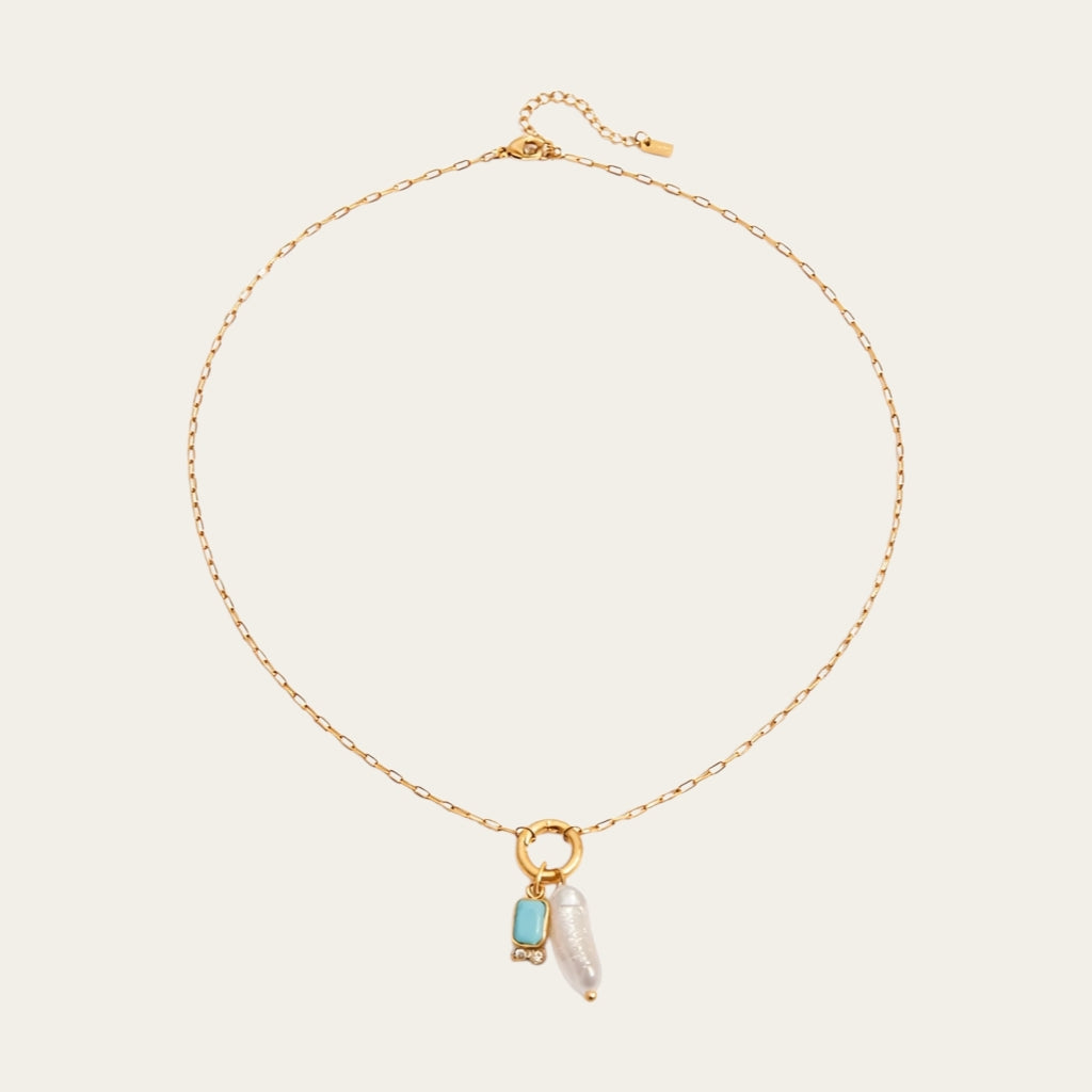 Fashionable gelaagde sieradenstijl met gouden schakelketting, parels en geboortestenen in verschillende kleuren.