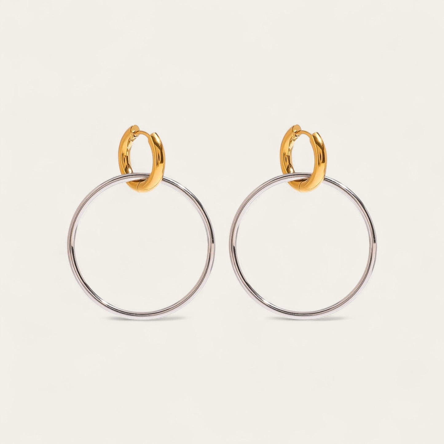 Paar bicolor hoop oorbellen met een kleine gouden huggie en een grote zilveren ring.