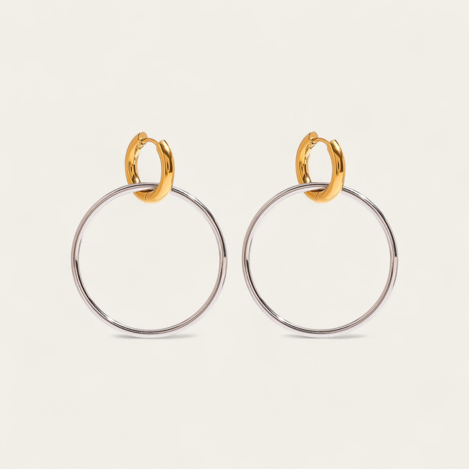 Paar bicolor hoop oorbellen met een kleine gouden huggie en een grote zilveren ring.