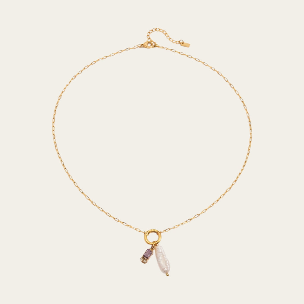 Fashionable gelaagde sieradenstijl met gouden schakelketting, parels en geboortestenen in verschillende kleuren.