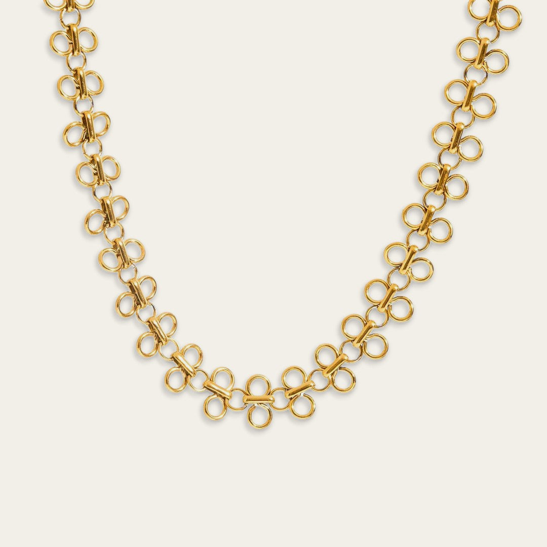 Close-up van de goudkleurige schakels van de filigraan choker. Het detail toont het fijne vlechtwerk van de ronde ringetjes en de glanzende afwerking van het metaal.