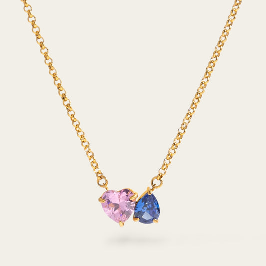 Gouden ketting met twee edelstenen: een lichtroze hartje en een donkerblauwe druppelvormige steen op een fijne schakelketting.