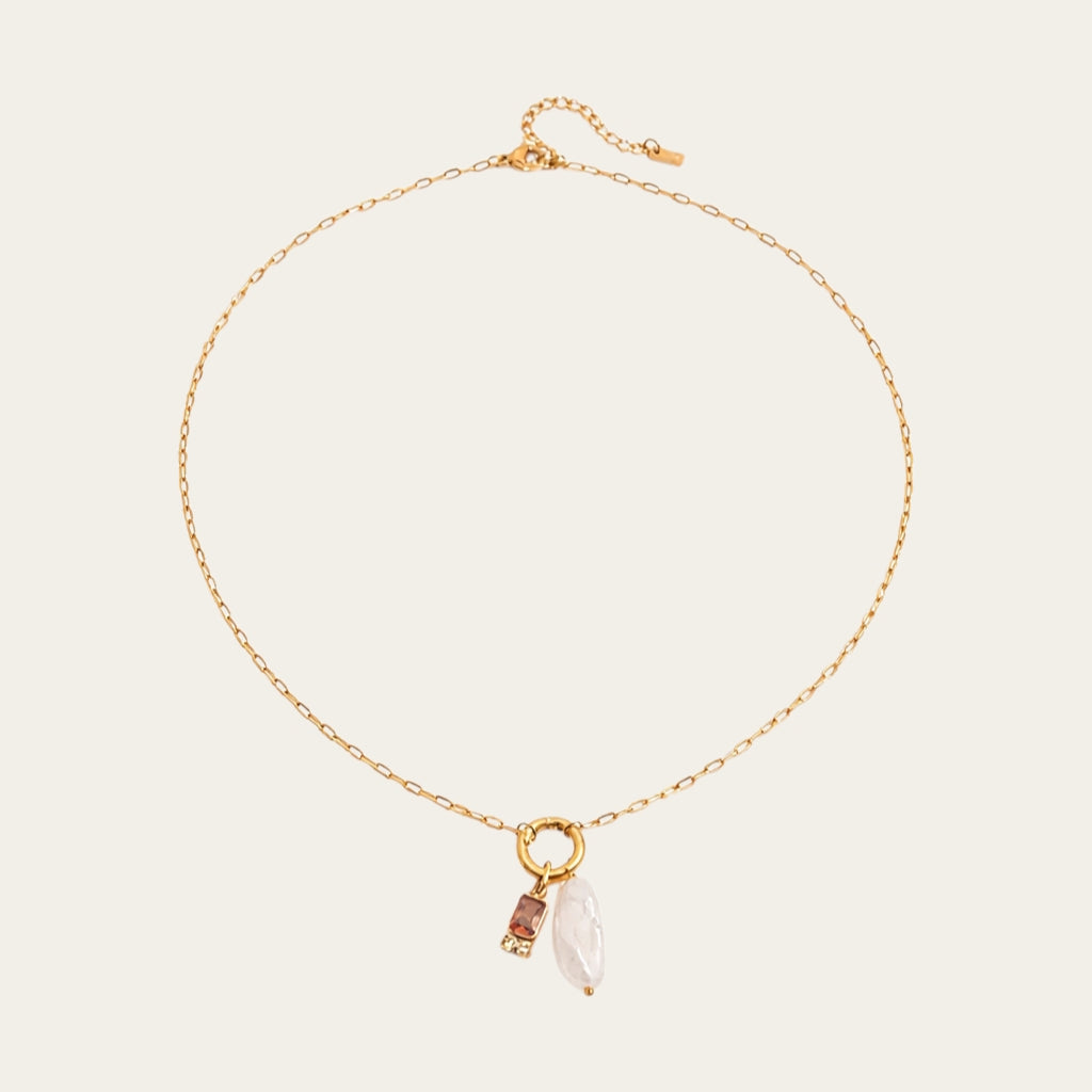 Fashionable gelaagde sieradenstijl met gouden schakelketting, parels en geboortestenen in verschillende kleuren.