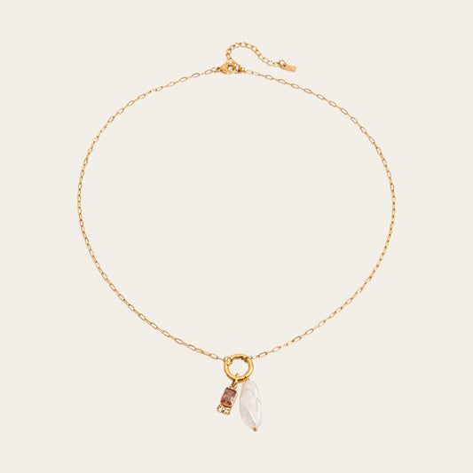 Fashionable gelaagde sieradenstijl met gouden schakelketting, parels en geboortestenen in verschillende kleuren.