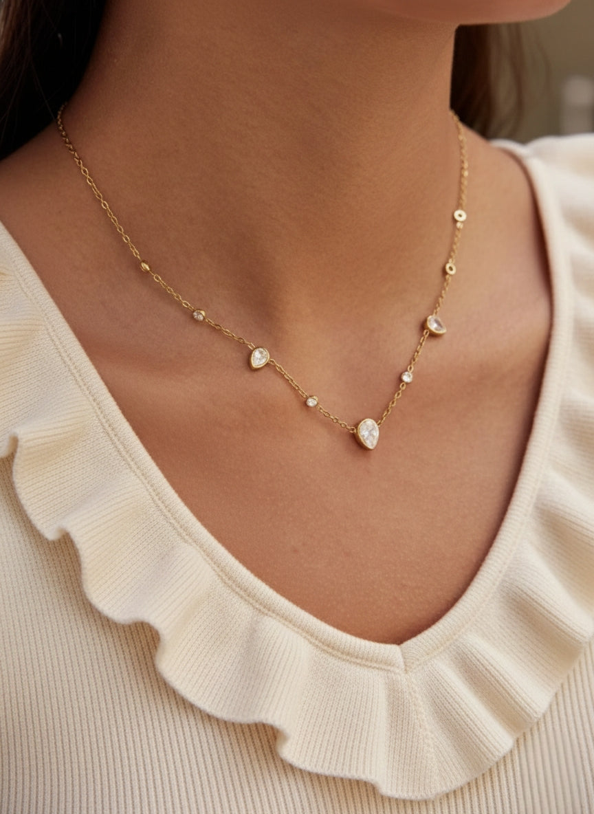 Model draagt een gouden sieraad met witte kristallen in druppelvorm en ronde zetting.