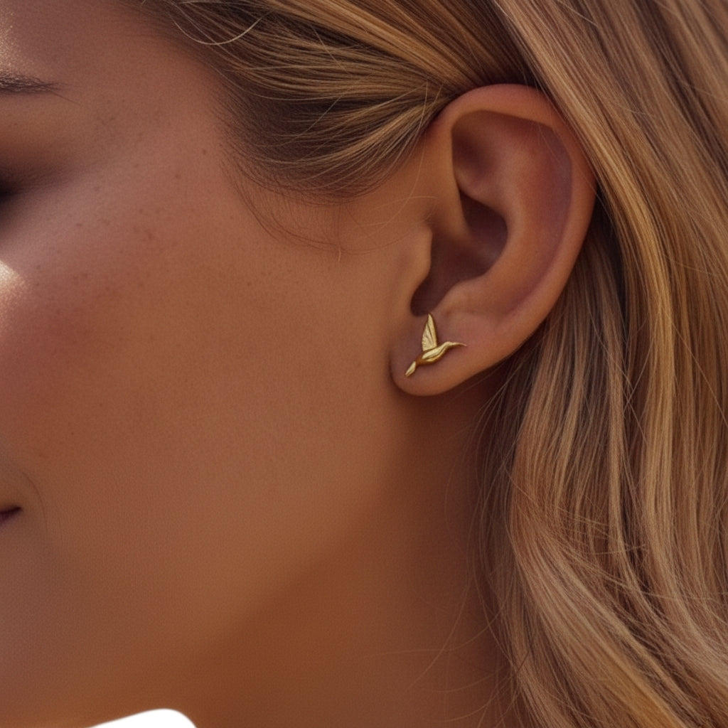 Model draagt minimalistische gouden oorknopjes in de vorm van een vliegende kolibrie voor een moderne ear-party.