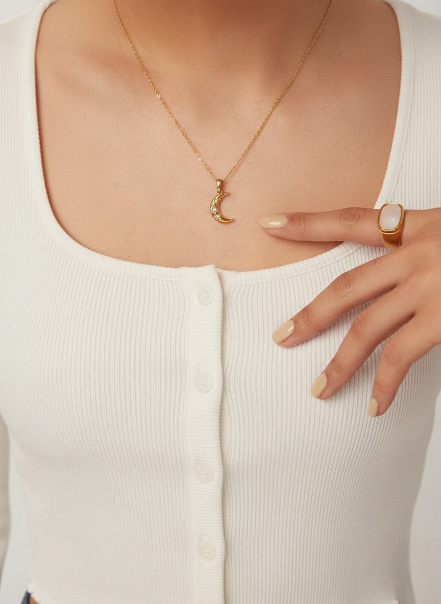 Model draagt een gouden schakelketting met verstelbare sluiting en een halve maan hanger met steentjes.
