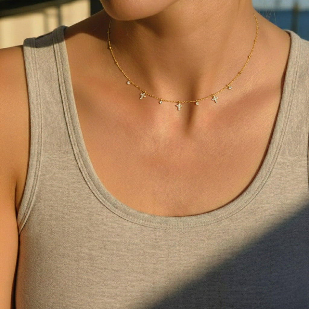 Model draagt een minimalistische gouden ketting met bedeltjes van kruisjes en zirkonia steentjes.