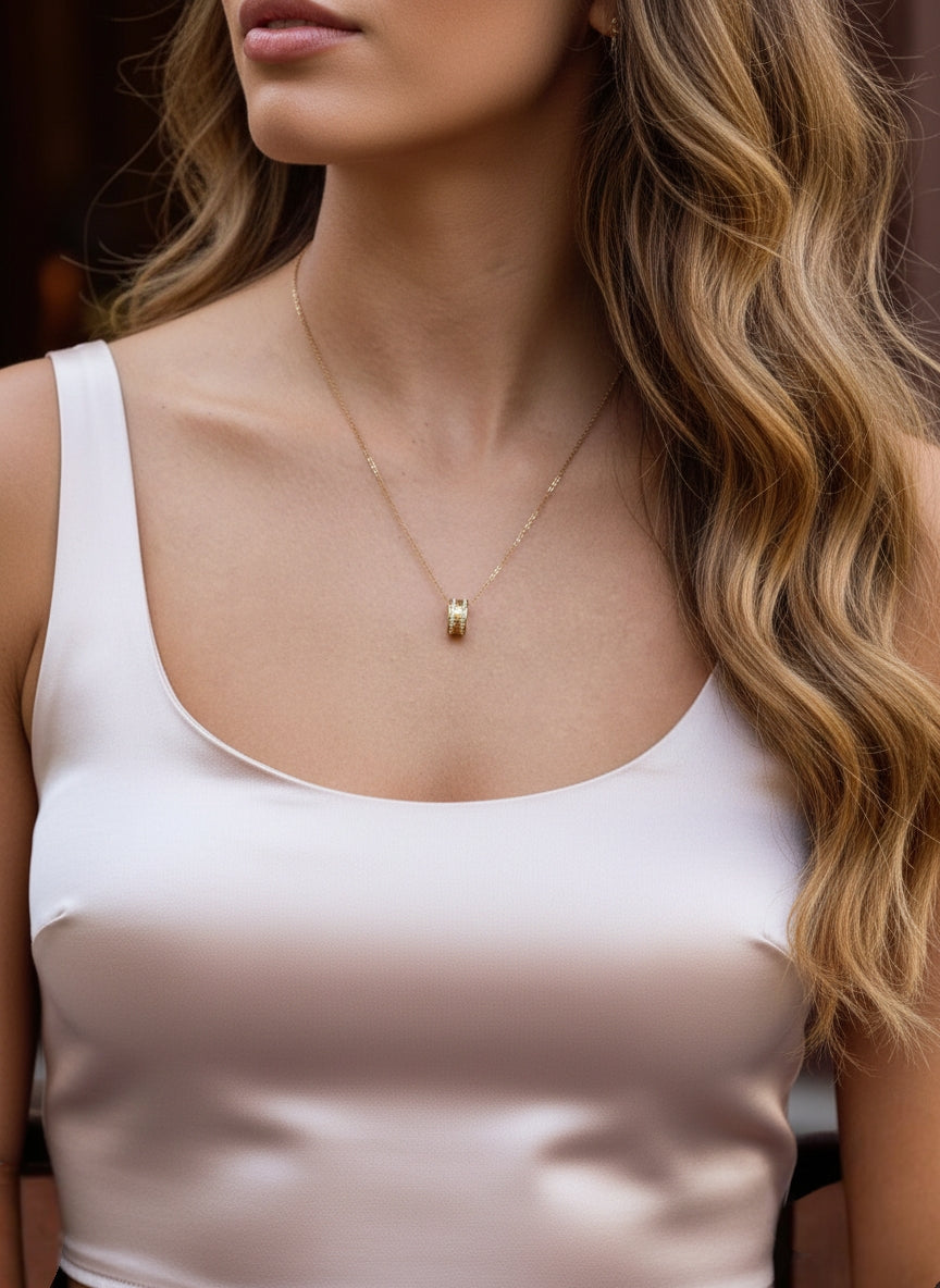 Minimalistische 'Mama' cilinder ketting van Cecelyn gedragen op een elegante satijnen top voor een modieuze look.