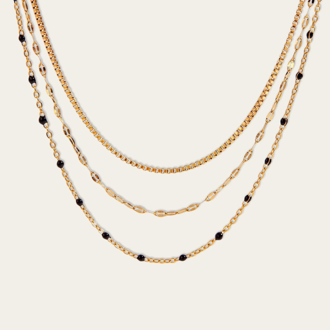 Detail van een elegante goudkleurige meerlaagse ketting met verschillende schakeldesigns en subtiele zwarte accenten.