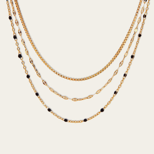 Detail van een elegante goudkleurige meerlaagse ketting met verschillende schakeldesigns en subtiele zwarte accenten.