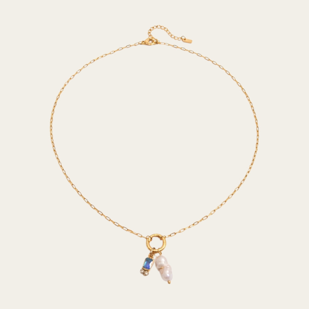 Fashionable gelaagde sieradenstijl met gouden schakelketting, parels en geboortestenen in verschillende kleuren.