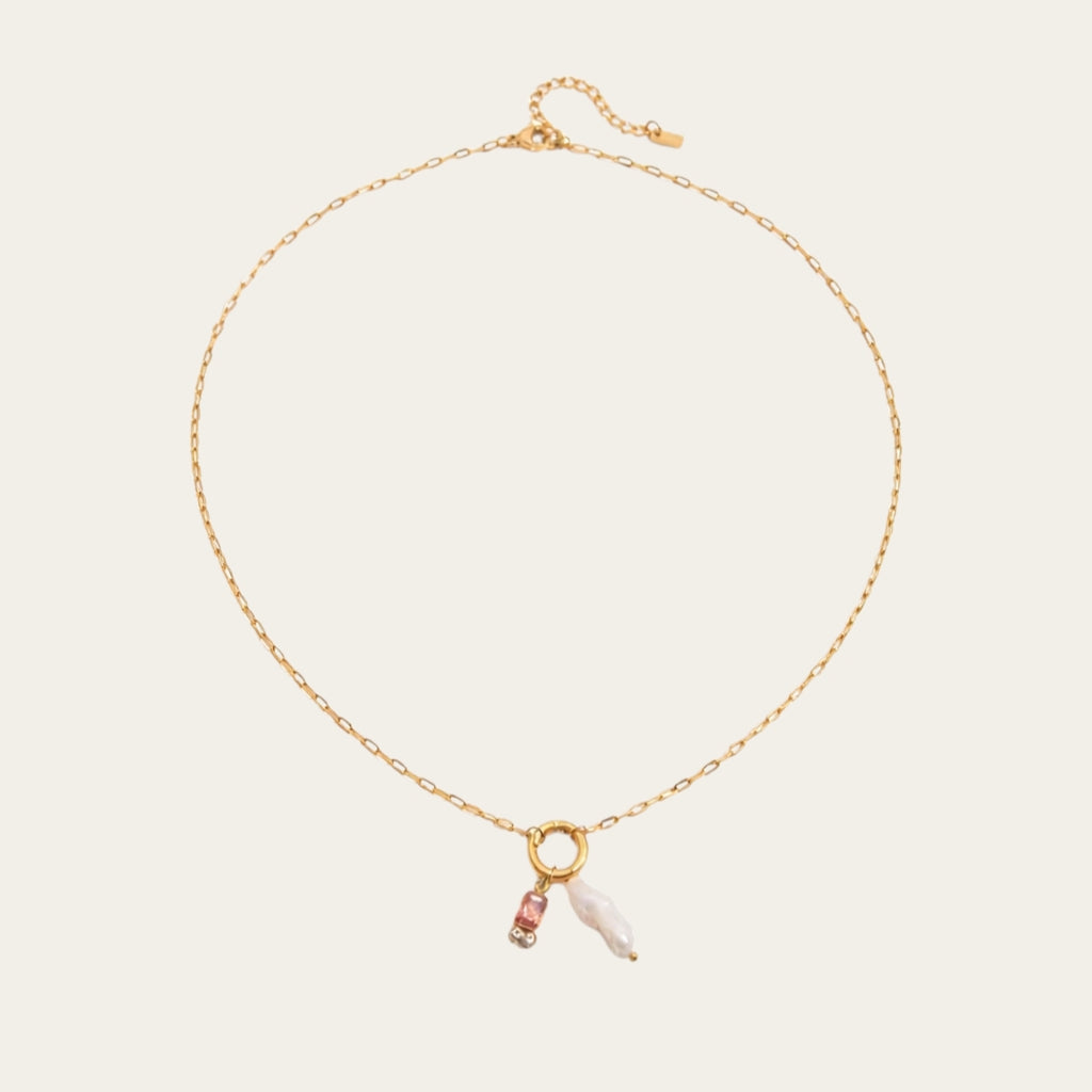 Fashionable gelaagde sieradenstijl met gouden schakelketting, parels en geboortestenen in verschillende kleuren.