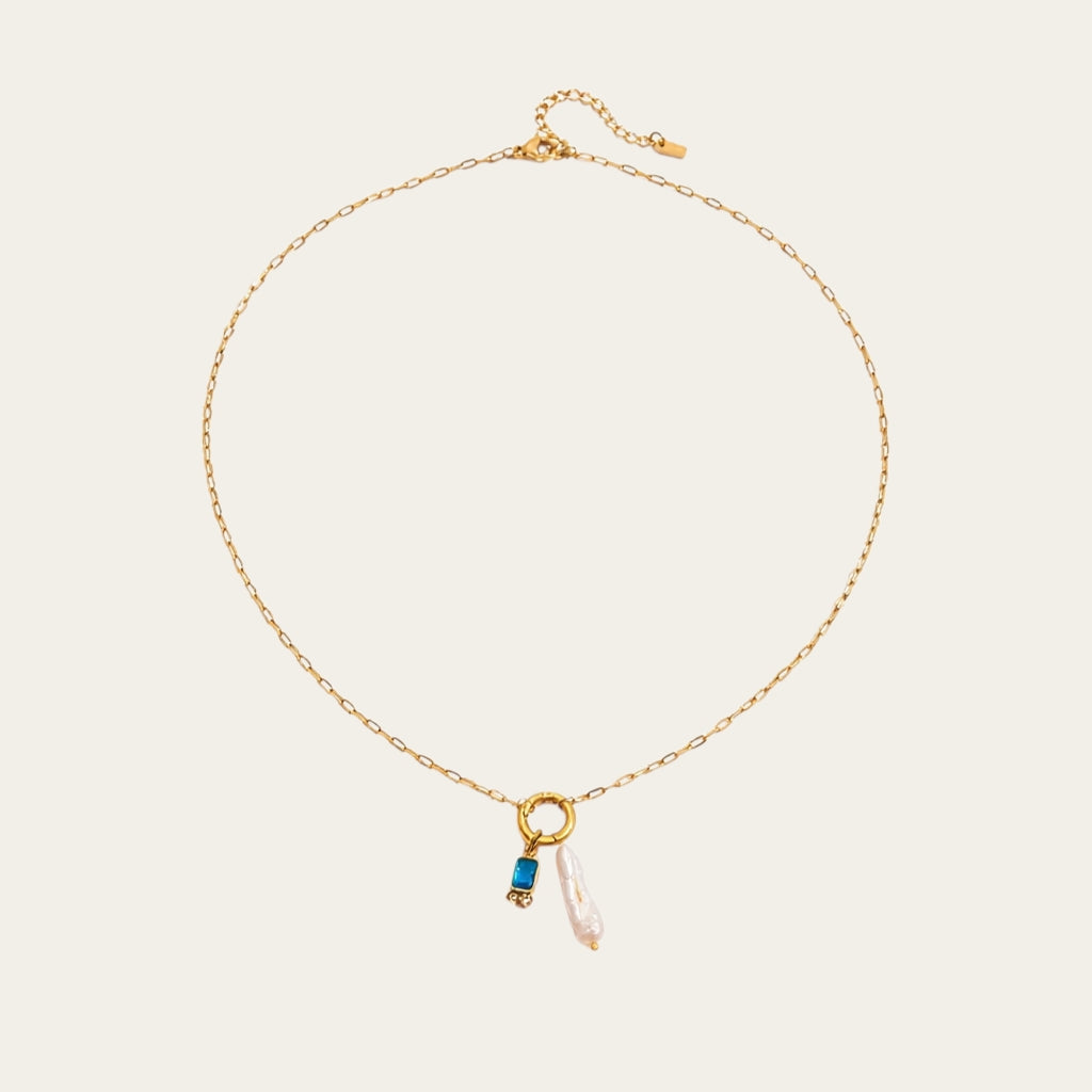 Fashionable gelaagde sieradenstijl met gouden schakelketting, parels en geboortestenen in verschillende kleuren.