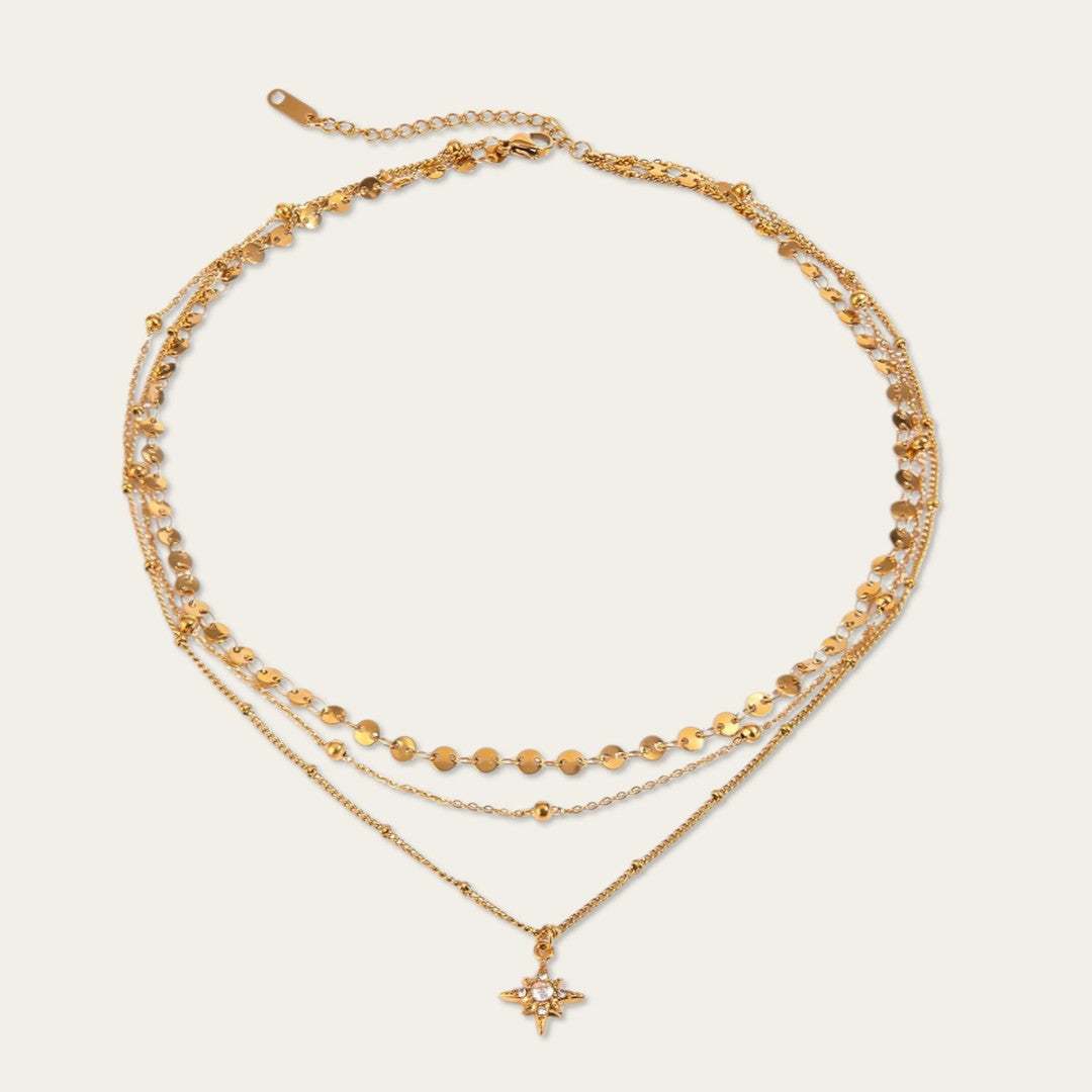 Gelaagde gouden ketting met drie lagen, kleine muntjes en een fonkelende ster-hanger.