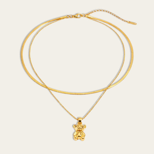 Gelaagde goudkleurige ketting met een gladde snake chain en een fijne bolletjesketting met een glanzende teddybeer hanger.
