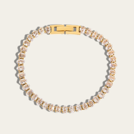Een gouden tennisarmband van CECELYN ingezet met een aaneenschakeling van glinsterende, ovaal geslepen zirkonia steentjes, voorzien van een strakke gouden kliksluiting en gefotografeerd tegen een witte achtergrond.
