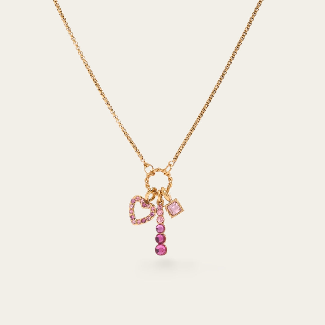 Goudkleurige ketting met drie roze bedeltjes: een hartje met kristallen, een roze steentje in vierkante zetting en een verticale rij roze strass-steentjes.